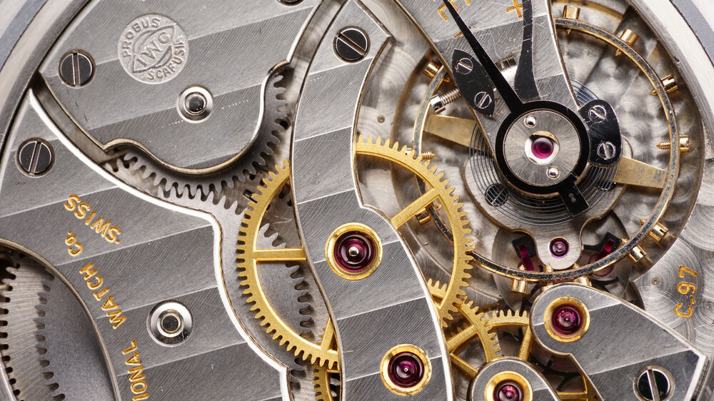 Detalle de mecanismo de reloj IWC de oro y plata con engranajes, rubíes y marcas de fabricante.