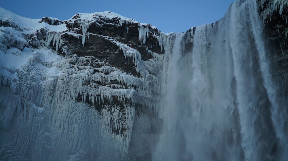 Cascada de Skogafoss, Islandia, con formaciones de hielo y un cielo azul pálido.