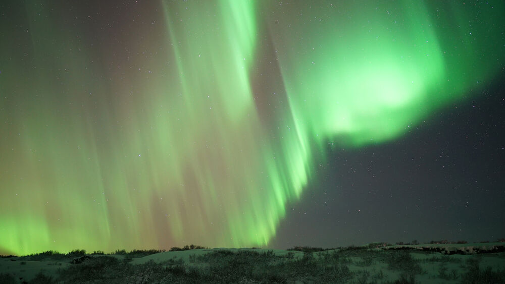Aurora boreal verde brillante sobre paisaje nevado nocturno con estrellas visibles.