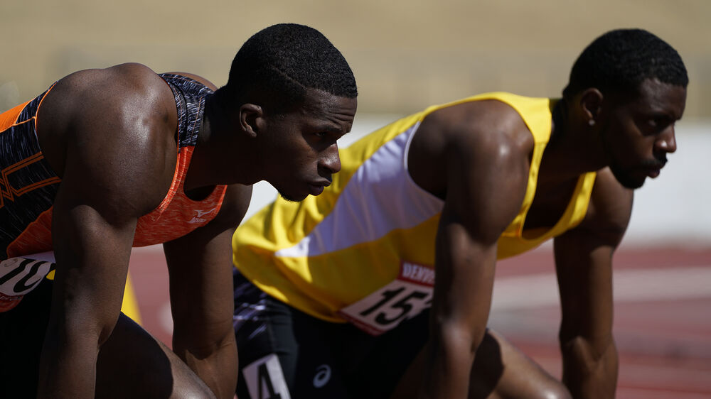 Corredores de atletismo en posición de salida en pista de color rojo, listos para comenzar la carrera.
