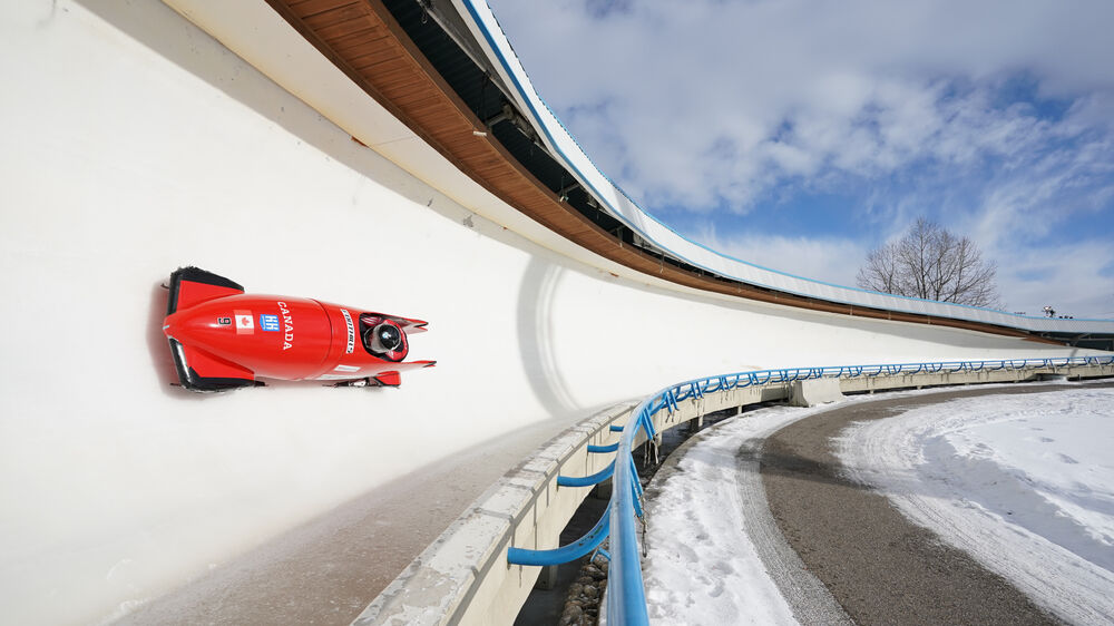Bobsleigh rojo de Canada número 6 en pista de hielo con cielo azul y nubes.