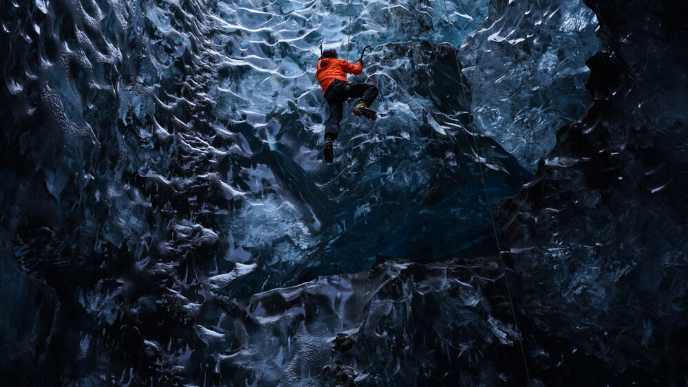 Escalador en cueva de hielo azul con equipo naranja, lente Sony FE 24-70mm f/2.8 GM.