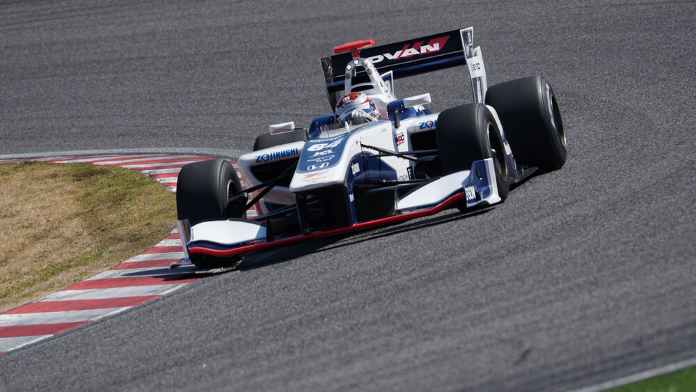 Automóvil de carreras blanco y azul con logo ADVAN en pista, girando en curva.