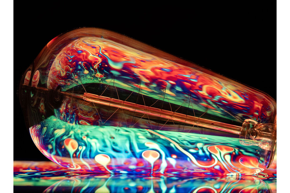 Lente macro FUJIFILM GF 120mm con filamentos incandescentes y reflejos abstractos multicolores.